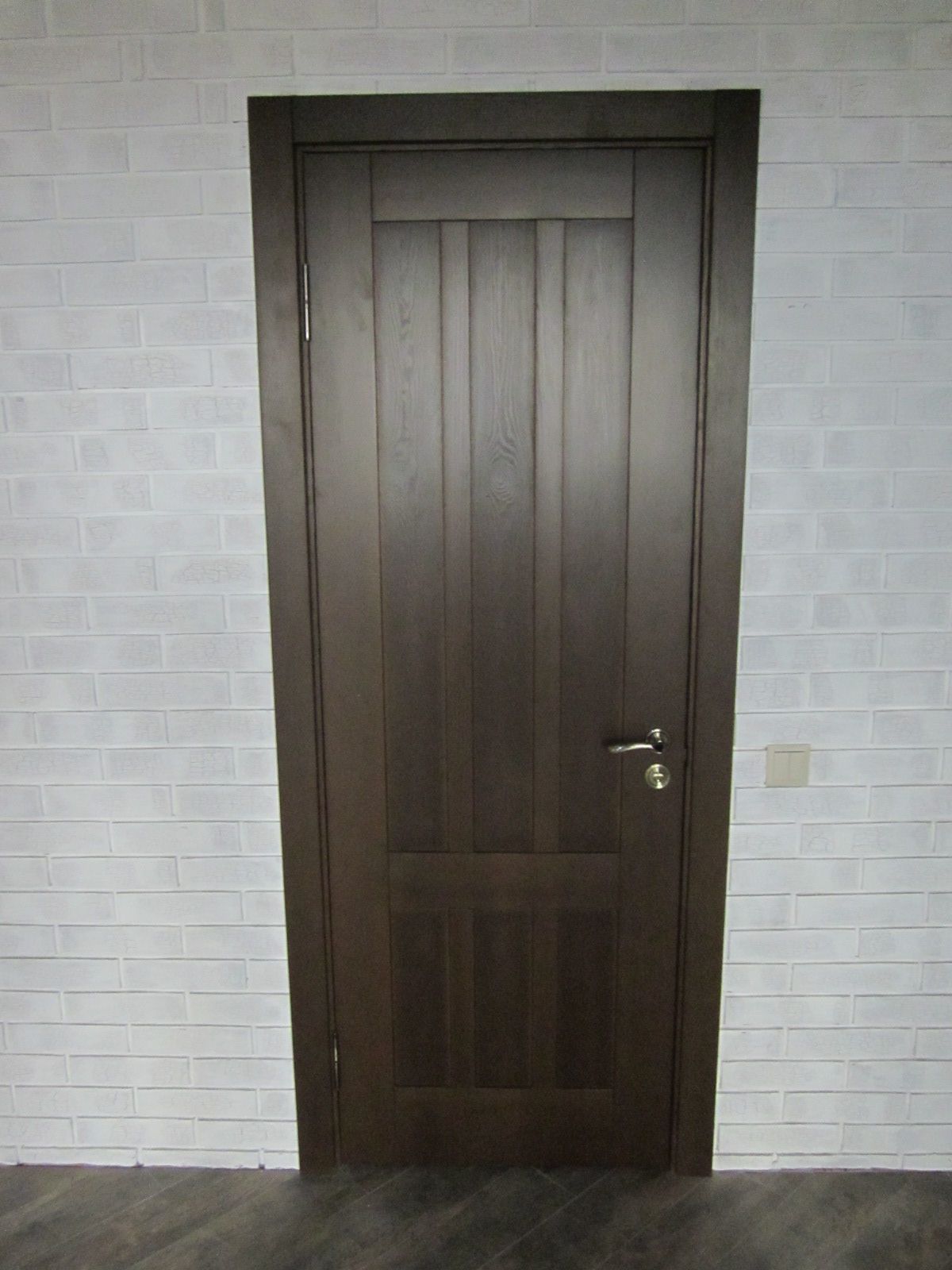 Dark wooden interior door and white brick wall